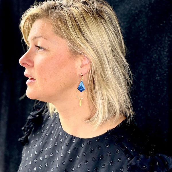 Boucle d'oreille Gali de Nune, dorée à l'or fin avec triangle de cuir marin, cuir de poisson saumon bleu saphyr métallisé, de forme grande goutte, portée à l'oreille