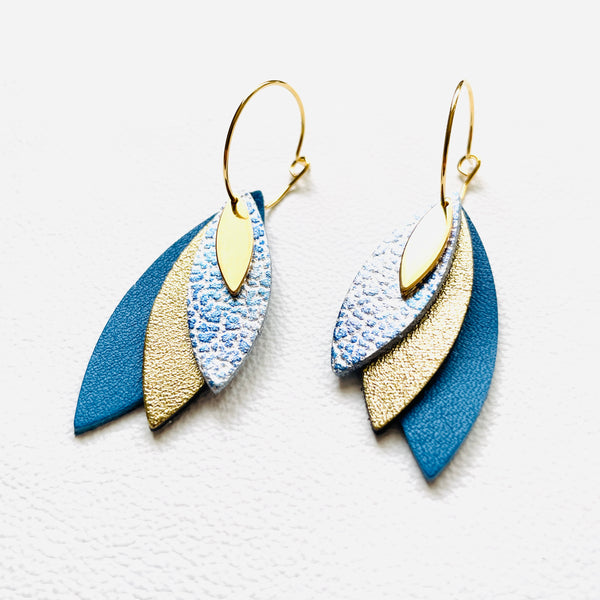 Boucles d'oreilles créoles dorées Nune modèle Piume en cuirs bleu ciel métal patiné, doré satiné et bleu denim mat sur fond blanc