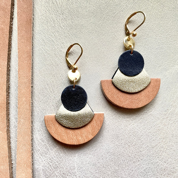 boucles d'oreilles dorées Nune modèle Hestia en cuirs beige amande, noir satiné et doré satiné sur fond gris doré