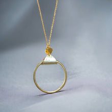 Charger l&#39;image dans la galerie, Collier fin dorée avec pendentif grand anneau créole attaché par une fine pièce de liège doré antique, sur fond gris
