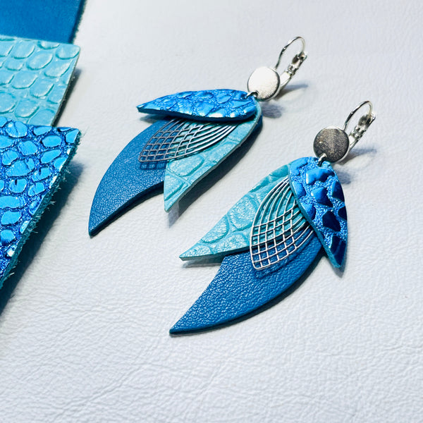 Boucles d'oreilles argentées Nune en forme de plumes, modèle Ara en cuirs bleu brillant façon croco, turquoise lézard et  bleu denim mat sur fond blanc