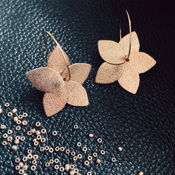 Nune petites boucles d'oreilles créoles Jasmin en cuir cannelle dorée satinée recyclé et anneaux dorés, vues de dessus, sur fond de cuir noir grainé