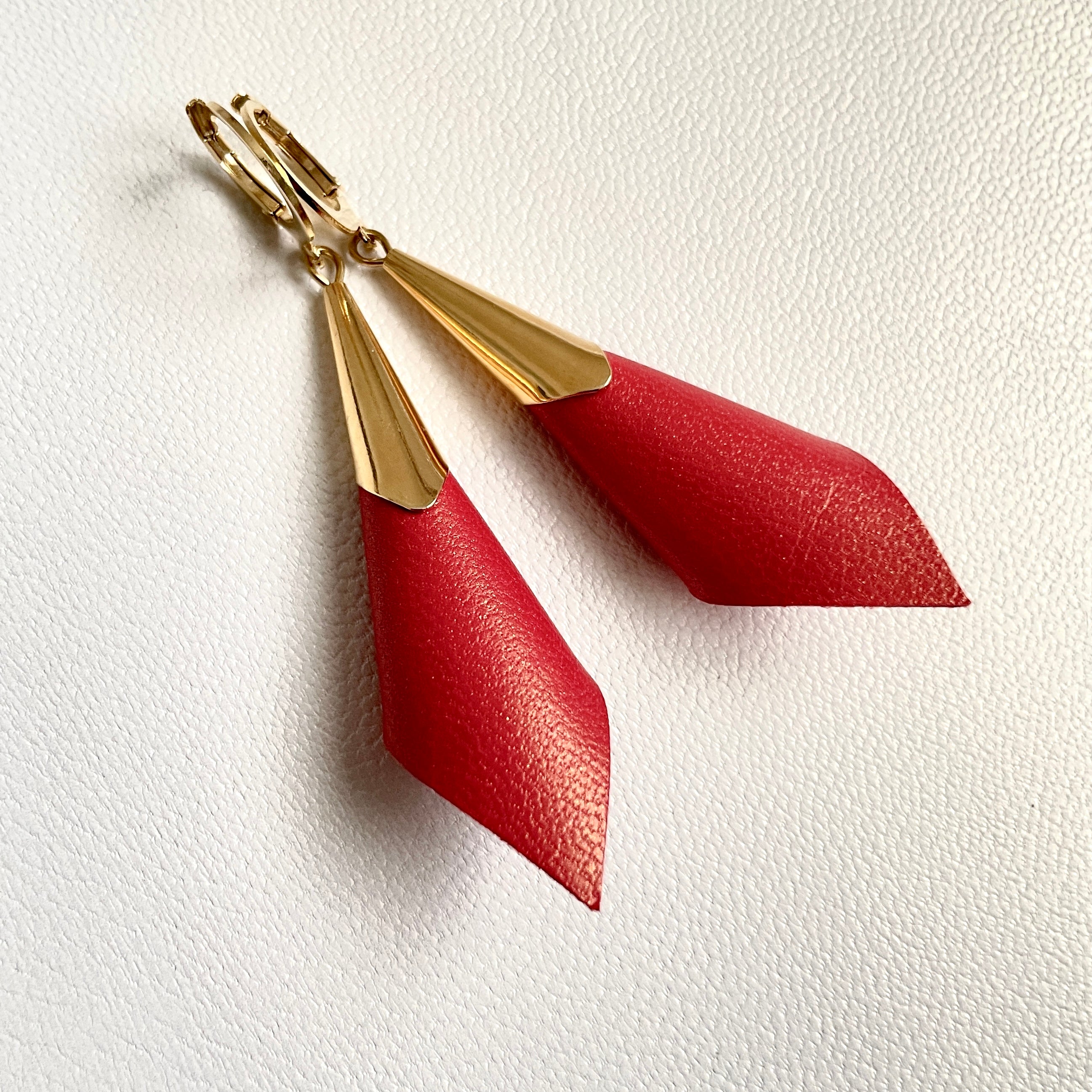 Boucles d'oreilles dorées Nune modèle Alice en forme de cônes de cuir rouge orangé nacré, sur fond cuir blanc cassé nacré