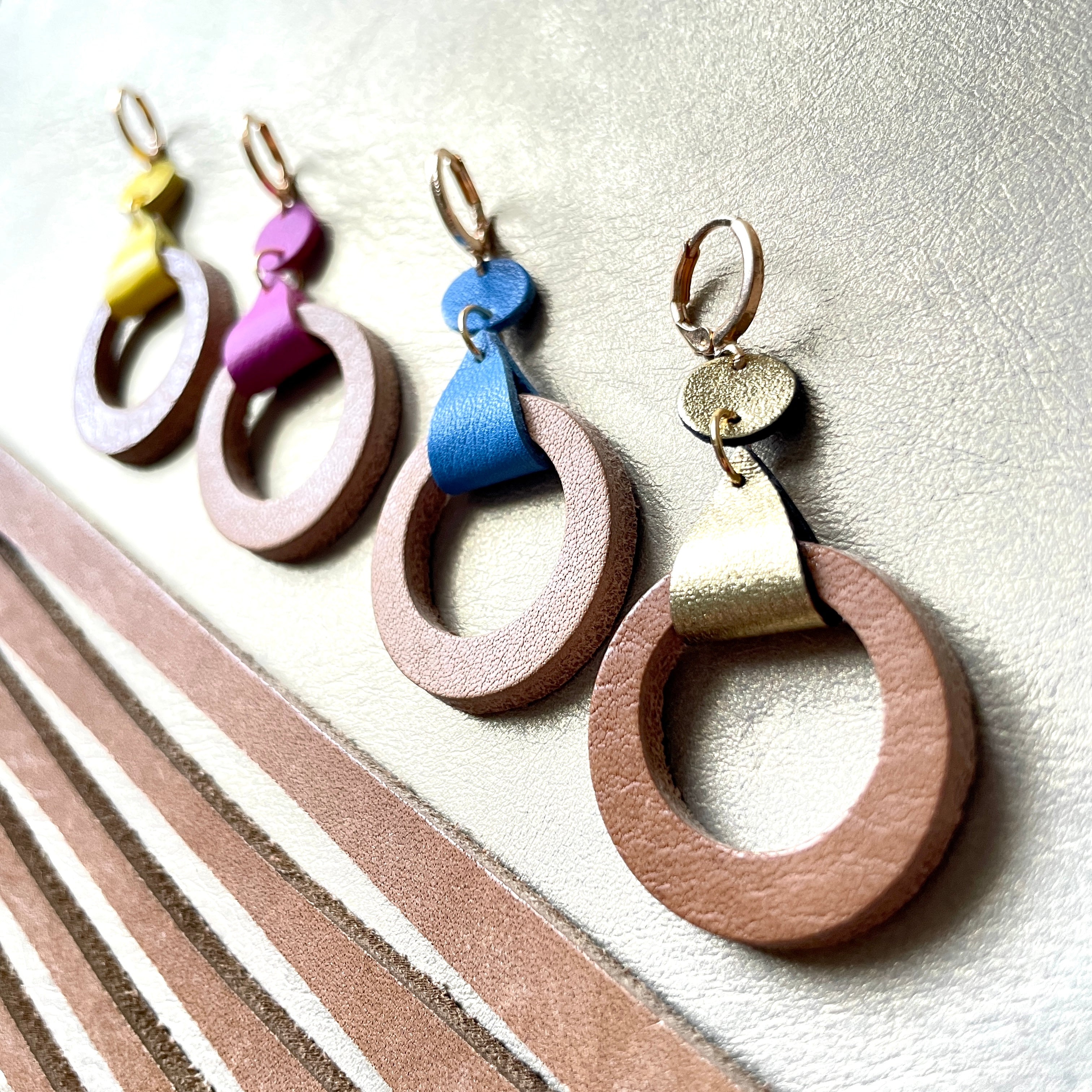 boucles d'oreilles dorées Nune modèle Cyllène en cuirs beige amande et doré satiné, bleu denim mat, mauve mat, jaune citron sur fond gris doré