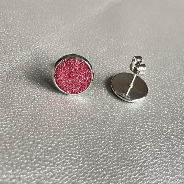Puces d'oreilles argentées rondes Nune modèle Ilis argenté pailleté avec pastilles de cuir framboise pailleté argent, sur fond de cuir gris métallisé